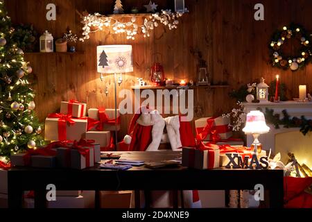 Santa costume hanging on chair at table with Merry Christmas decor in cozy home. Stock Photo