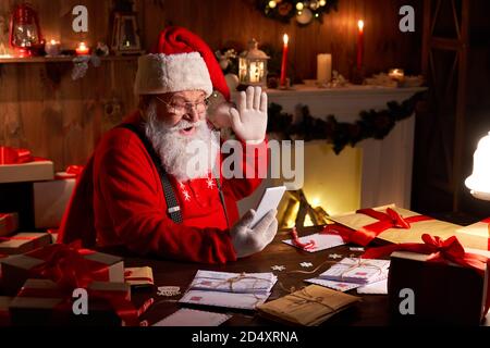 Santa Claus video calling child on smartphone sitting at home table. Stock Photo