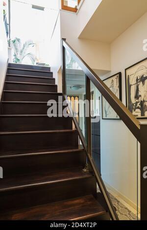 Looking up brown stained and varnished oak wood stairs leading from basement to ground floor inside contemporary home decorated with drawings. Stock Photo