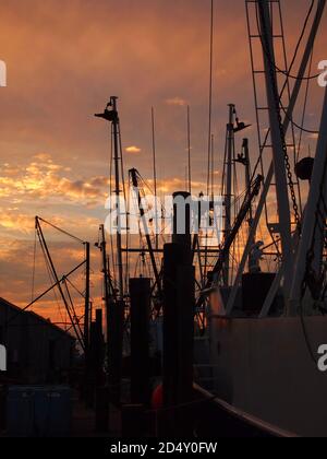 Fishing boat rigging in deep silhouette after sunset against a warm sky with red, yellow and orange clouds. Stock Photo