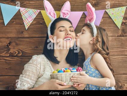Mother and her daughter with painting eggs. Happy family celebrate Easter. Cute little child girl wearing bunny ears. Stock Photo