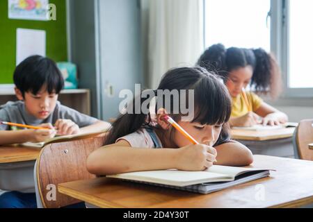 School girl sitting in school writing in book with pencil, studying, education, learning. Asian children in the class. Student diversity. Stock Photo