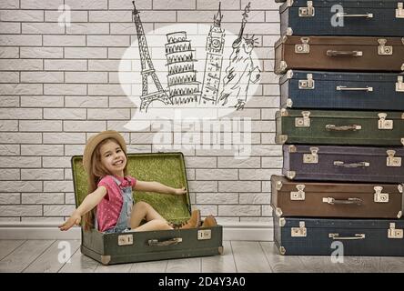 happy child girl against a white brick wall. girl having suitcases and dreaming of traveling. Stock Photo