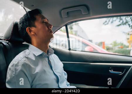 Tired businessman asleep in back seat of car, resting, on the move, business travel, sleeping Stock Photo