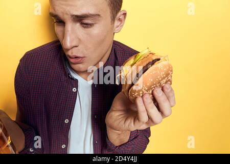 Cheerful man with a mug of beer and a hamburger on his hands diet food lifestyle yellow background Stock Photo