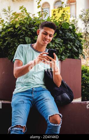 Vertical shot of a young Hispanic man sitting while texting through his phone Stock Photo