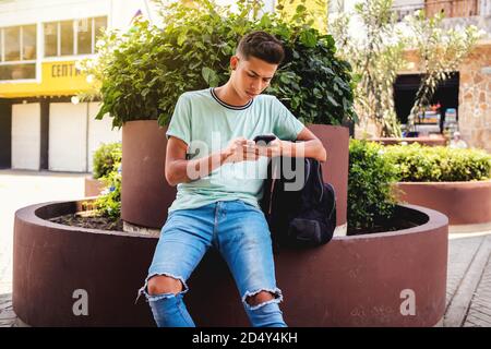 Young Hispanic man sitting while texting through his phone Stock Photo
