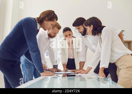 Team of office workers together with boss leaning over table studying documents and reports Stock Photo