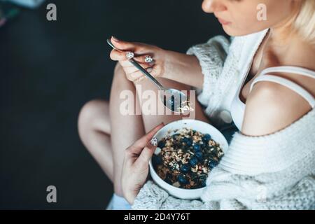 Upper view photo of a caucasian woman in a knitted sweater eating cereals with berry at home Stock Photo