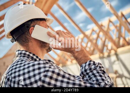 Dark-haired young builder in a protective helmet making a phone call Stock Photo