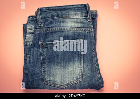 Blue frayed jeans with a pocket, folded shabby pants on a pink background. Dark denim Stock Photo