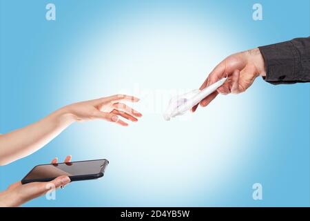 A man gives a woman a package of wet antibacterial wipes to wipe the smartphone with. Hands are close-up on a blue background. The concept of disinfec Stock Photo