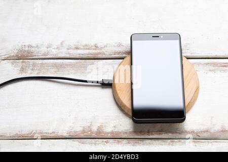 Concept of modern technologies. On the wireless charger is a black smartphone with a glossy white screen. White wooden background with horizontal stri Stock Photo