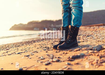 Close-up of women's feet in black casual shoes, standing on the sand of the beach, autumn or winter. Copy space. Stock Photo