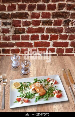 Rustic wooden table with a set of silverware , White plate with shrimp and cheese croquettes on tomato and salad. Stock Photo