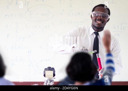 Science african teacher standing in front of blackboard teaching student in classroom Stock Photo