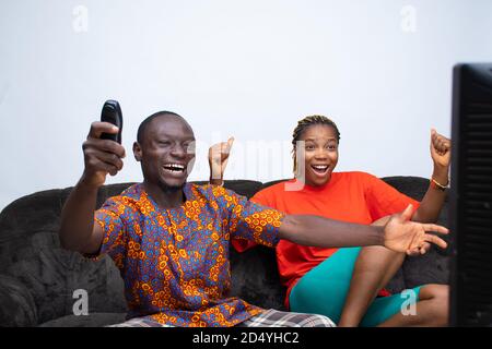 young african couple watching television together excitedly cheering and supporting their team Stock Photo