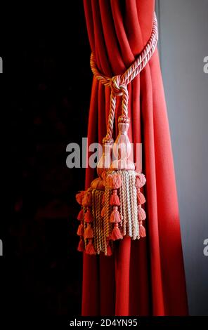 sumptuous red velvet curtain fabric and decorative cord rope tassels in period english home interior Stock Photo
