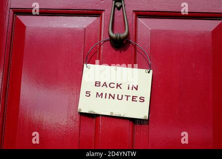 back in 5 minutes sign on red wooden door Stock Photo