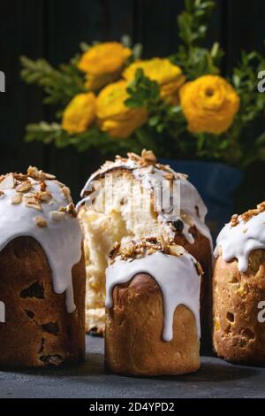 Set of traditional Russian and Ukrainian Easter cake Kulich Paska bread glazed with almond, whole and sliced, served with yellow flowers, colored eggs Stock Photo