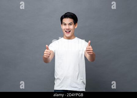 Handsome Asian man smiling and giving thumbs up on gray isolated backround Stock Photo