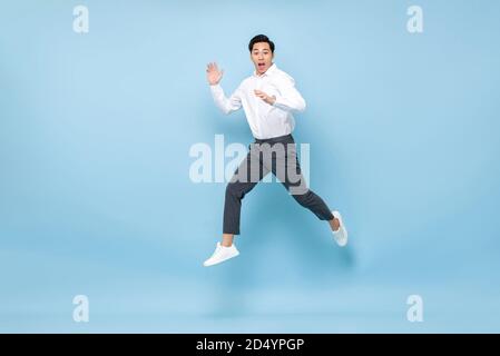 Energetic Asian man in semi formal clothes jumping in mid air isolated on light blue background Stock Photo