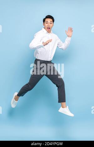 Energetic Asian man in semi formal clothes jumping in mid air isolated on light blue background Stock Photo