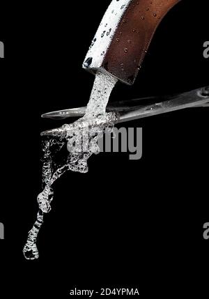 Scissors cut a stream of clean, cold water from a misted tap. Stock Photo