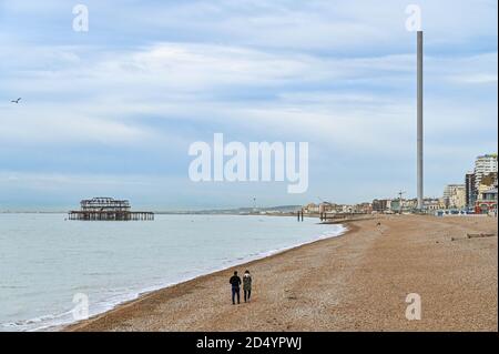 Brighton UK 12th October 2020 - A couple out walking along Brighton beach which is quiet on an overcast dull day on the South Coast . : Credit Simon Dack / Alamy Live News Stock Photo