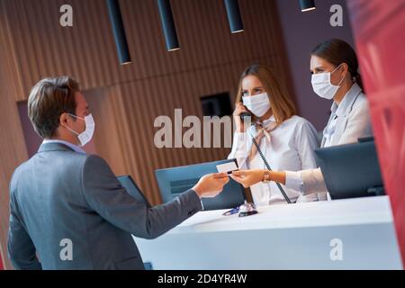 Businessman in mask at the reception of a hotel checking in Stock Photo