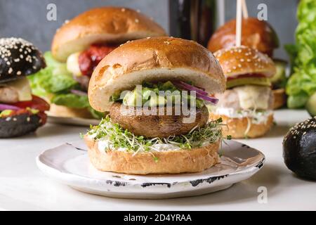 Variety of homemade classic, vegan and mini burgers in wheat and black buns with beef and veal cutlets, portobello mushroom, avocado on white ceramic Stock Photo