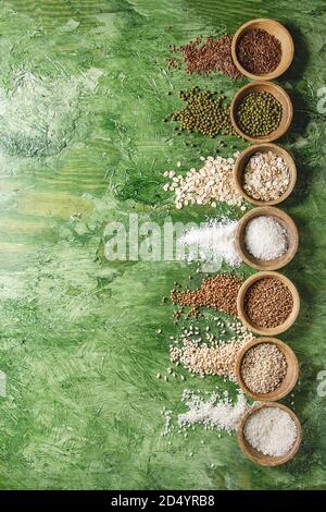 Variety of raw uncooked grains superfood cereal linen seeds, sesame, mung bean, wheat, buckwheat, oatmeal, coconut, rice in wooden bowls over green te Stock Photo