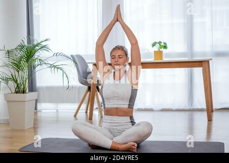 Beautiful active young woman workout at home. Meditating in yoga asana lotus pose. Healthy lifestyle and fitness concept. Series of exercise poses. Stock Photo