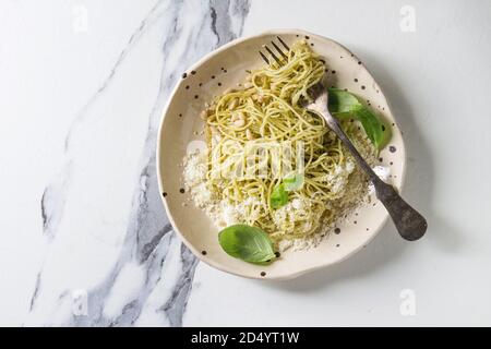 Classic italian spaghetti pasta with pesto sauce, pine nuts, olive oil and fresh basil. Served in ceramic plate with fork over white marble background Stock Photo
