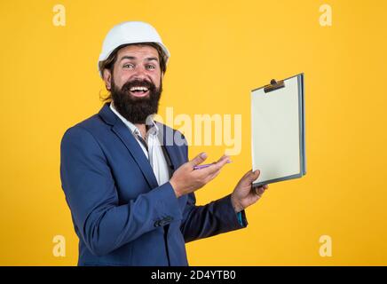 Safety expert. building concept. builder or engineer in hard hat. happy mature architect in helmet making notes. brutal bearded man work on construction site with documents. working on project. Stock Photo