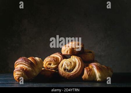Variety of homemade puff pastry buns cinnamon rolls and croissant on wooden table. Dark still life. Copy space Stock Photo