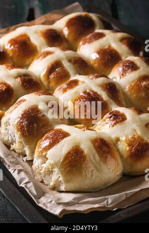 Homemade Easter traditional hot cross buns on oven tray with baking paper over dark wooden background. Close up Stock Photo