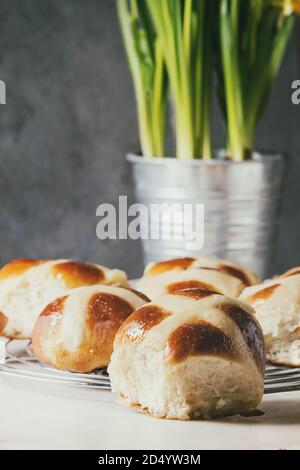 Homemade Easter traditional hot cross buns on cooling rack on white marble table with narcissus flowers. Stock Photo