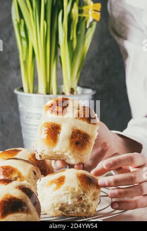 Child hands take homemade Easter traditional hot cross buns on cooling rack on white marble table with narcissus flowers. Stock Photo
