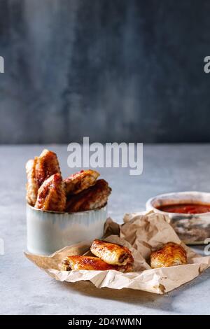 BBQ spicy chicken wings served in ceramic bowl and on paper with red sauce on light blue table. Stock Photo