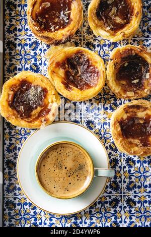Traditional Portuguese egg tart dessert Pasteis Pastel de nata in classic tile tray with cup of black coffee. Flat lay, space Stock Photo