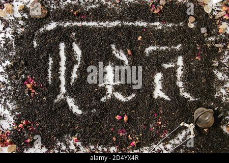 Calligraphic inscription gothic letters tea over dry black ceylon and green tea scattered on white marble with rose buds and stainer. Tea drinking con Stock Photo