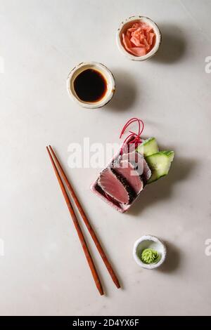 Tuna Sushi sashimi with cucumber in pink ceramic serving plate with chopsticks, bowls of soy sauce, and pickled ginger, cotton flowers over white marb Stock Photo