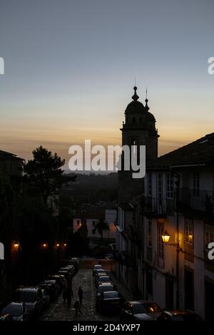 Santiago de Compostela, Galicia, Spain - 09/27/2020: Convento de San Francisco at sunset with a dimly sit street in front as people walk up it. Spain