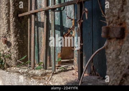 Broken and worn Spanish wooden shuttered window with rusted metal bars covering it set into a stone wall. Stock Photo