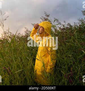 Man in yellow raincoat with the hood standing in wet reeds in rainy weather, side view. Autumn time Stock Photo