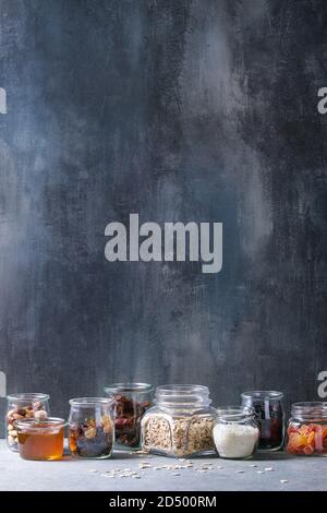 Variety of dried fruits, nuts, honey and oat flakes in different glass jars for cooking homemade healthy breakfast muesli or granola energy bars on gr Stock Photo