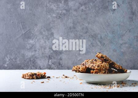 Homemade energy oats granola bars with dried fruits and nuts whole and broken in ceramic plate on grey table. Healthy snack. Stock Photo