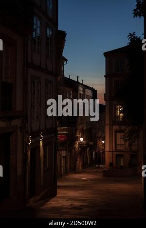 Rustic quiet narrow street lamp lit street in the old town of Santiago de Compostela at twilight. Galicia, Spain. Stock Photo