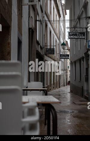 Santiago de Compostela, Galicia, Spain - 09/26/2020: Stacked plastic chairs and tables in a narrow empty hostel street with a closed cafe. Stock Photo